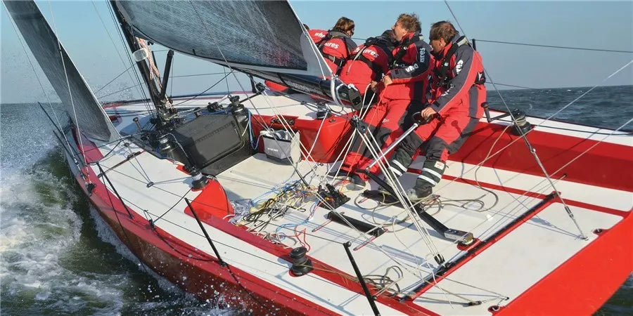 Crew in red sailing gear racing a modern red sailboat with sailing hardware and electronics on deck